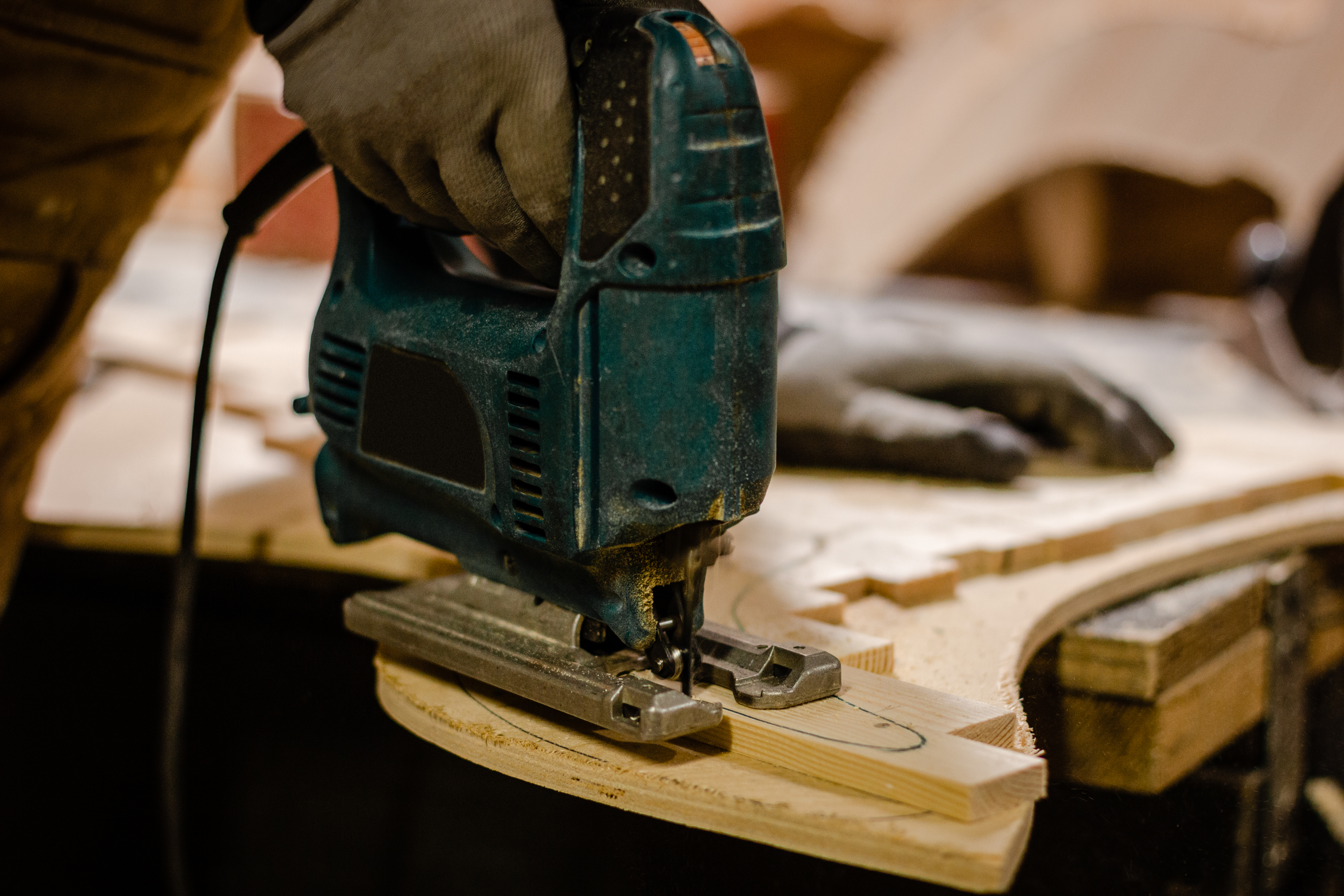 Carpenter cutting wooden parts with an electric jigsaw at the workshop